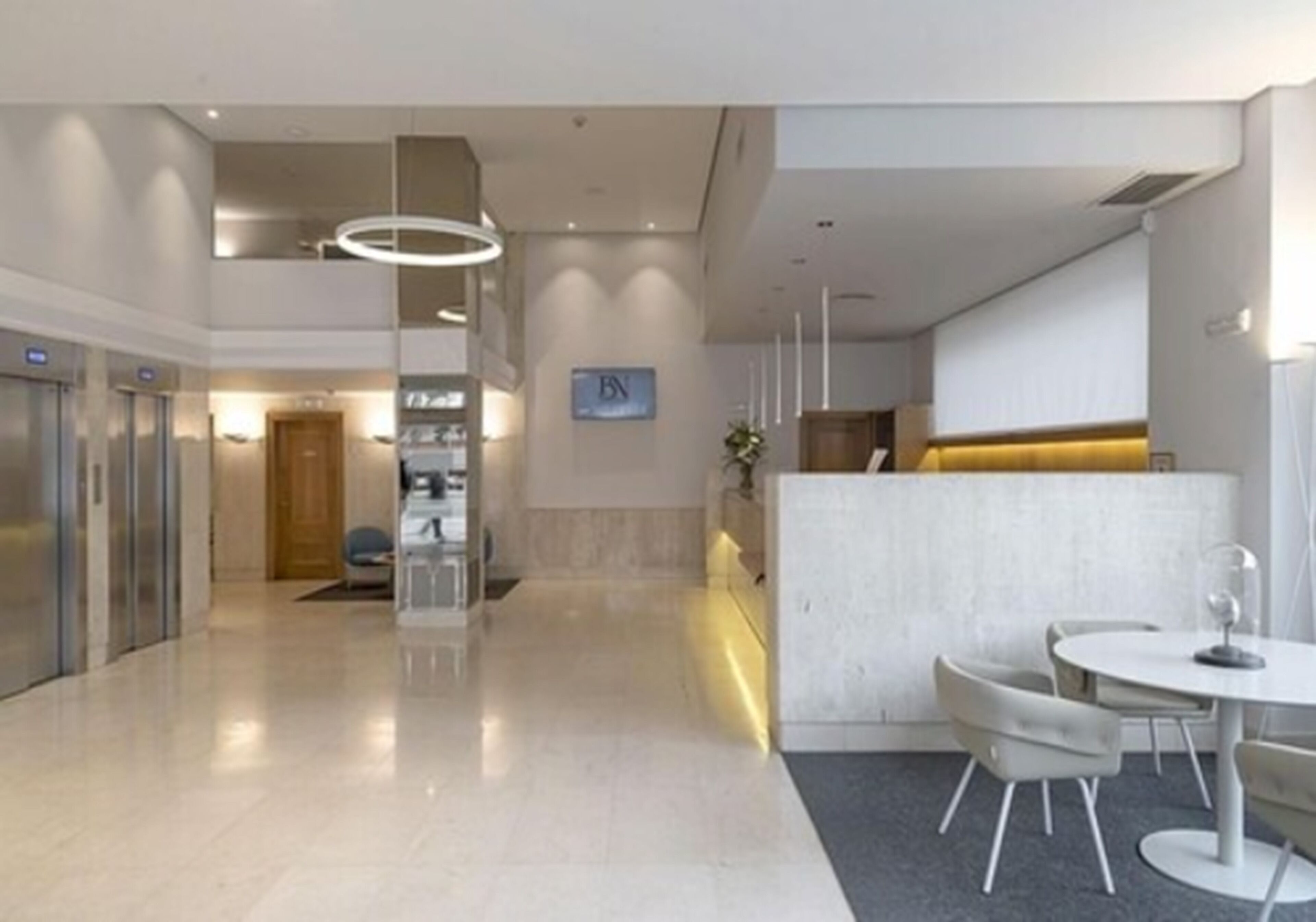 A modern hotel lobby with a reception desk, seating area, and elevators.