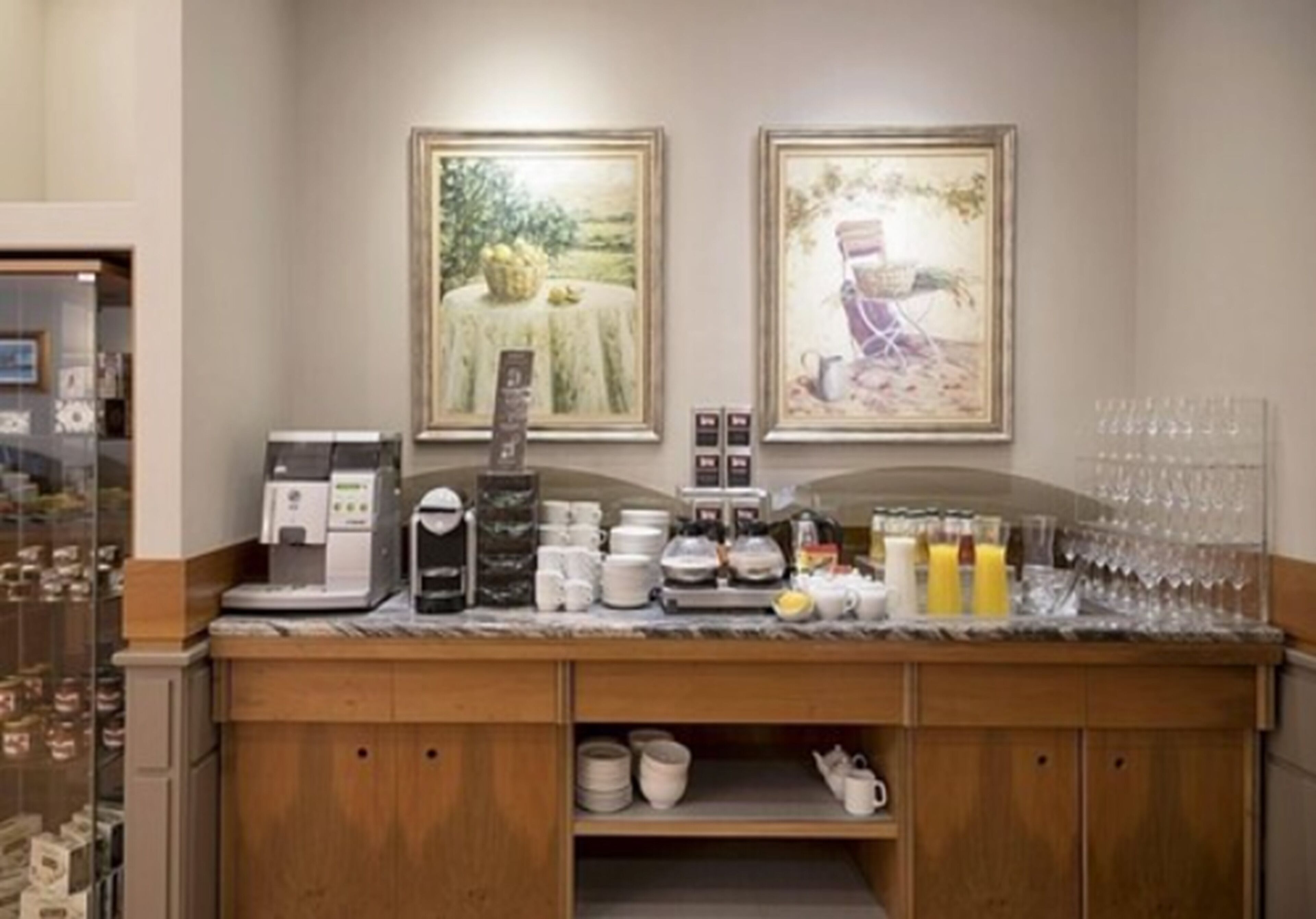 Zona de recepción de un hotel con máquina de café, estación de té y un estante para cristalería.