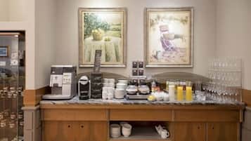 Zona de recepción de un hotel con máquina de café, estación de té y un estante para cristalería.