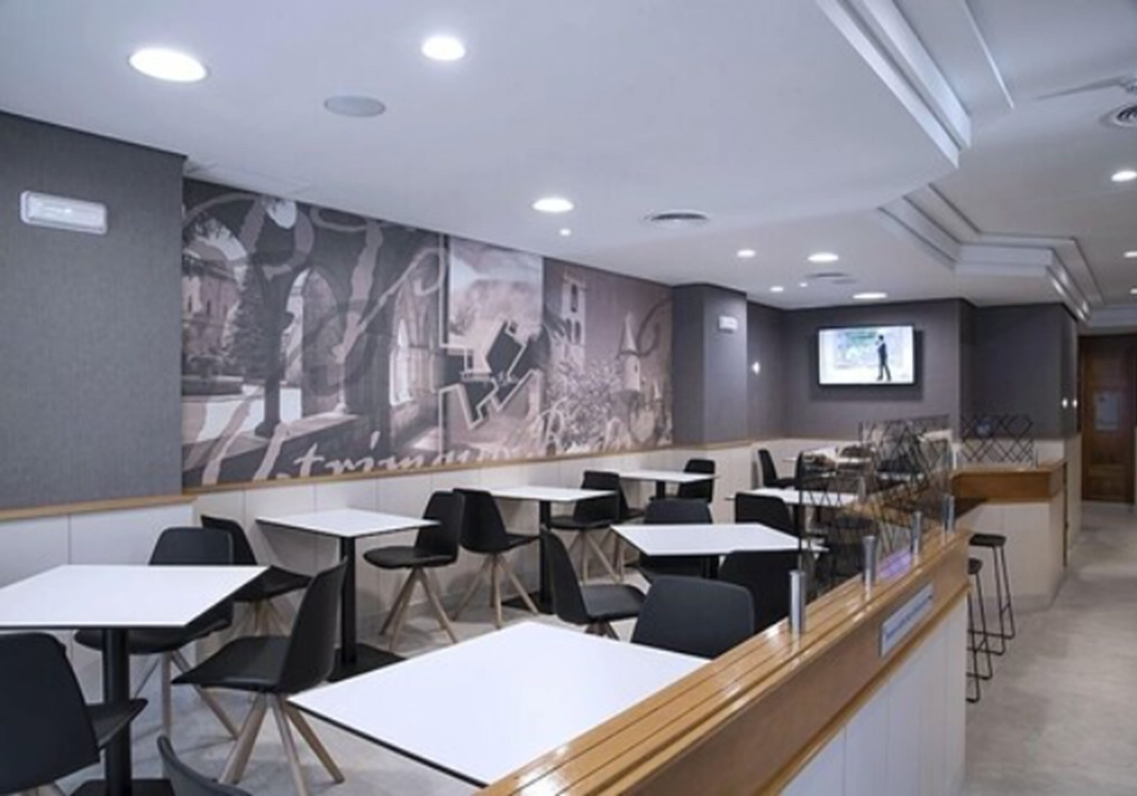Un área de comedor moderna con mesas y sillas, una barra con un menú a la vista y un mural en la pared.