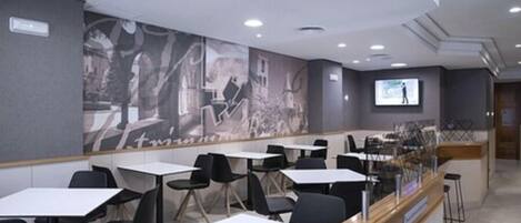 A modern dining area with tables and chairs, a counter with a menu display, and a mural on the wall.