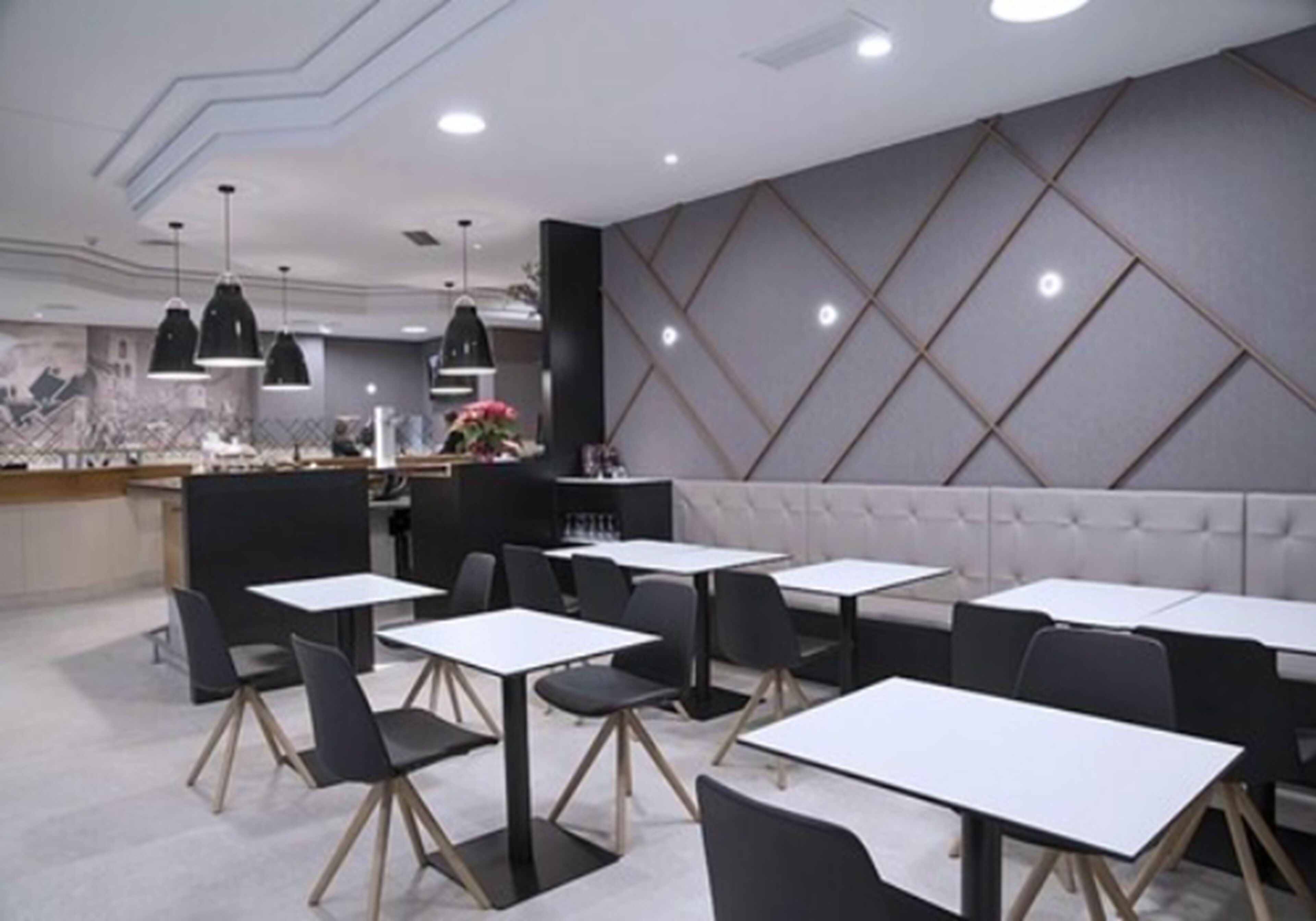 A modern restaurant with black and white tables and chairs, a bar area, and a patterned wall.