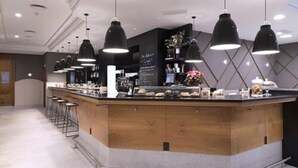 Un espace bar moderne doté d’un comptoir central, de tabourets de bar, de luminaires suspendus et d’un menu écrit à la craie.