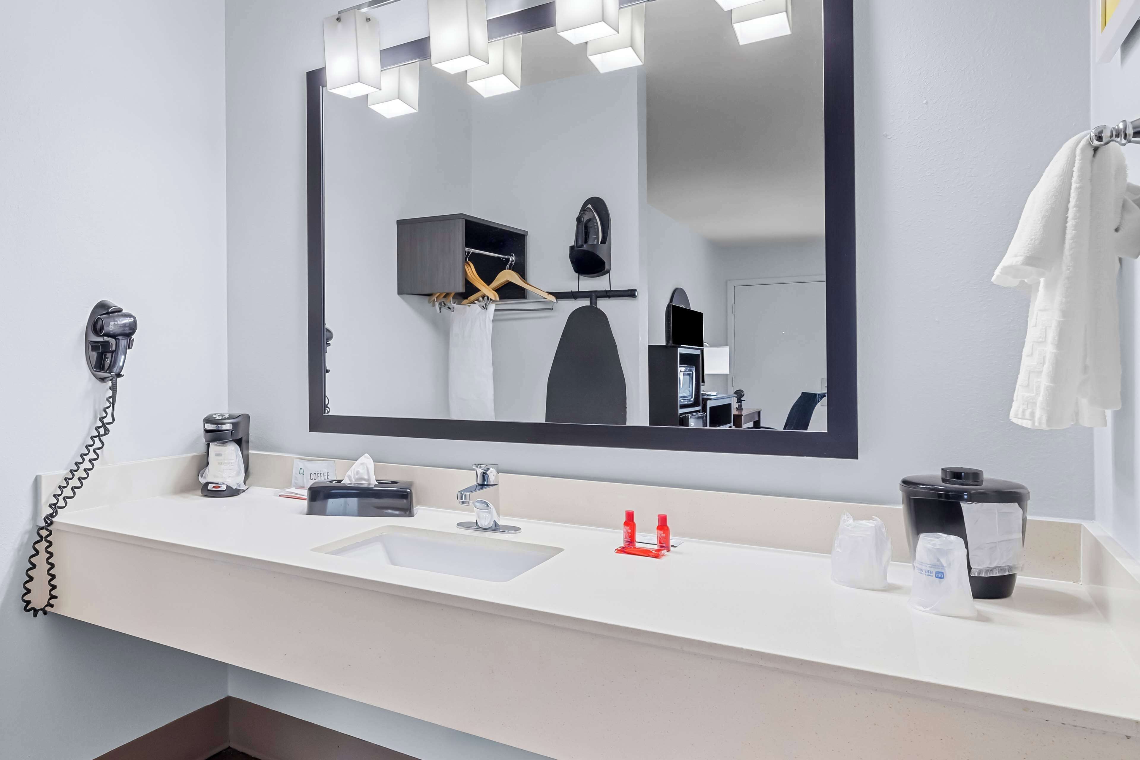 Un baño de hotel moderno con un espejo grande, un lavabo, un secador de pelo y una cafetera.