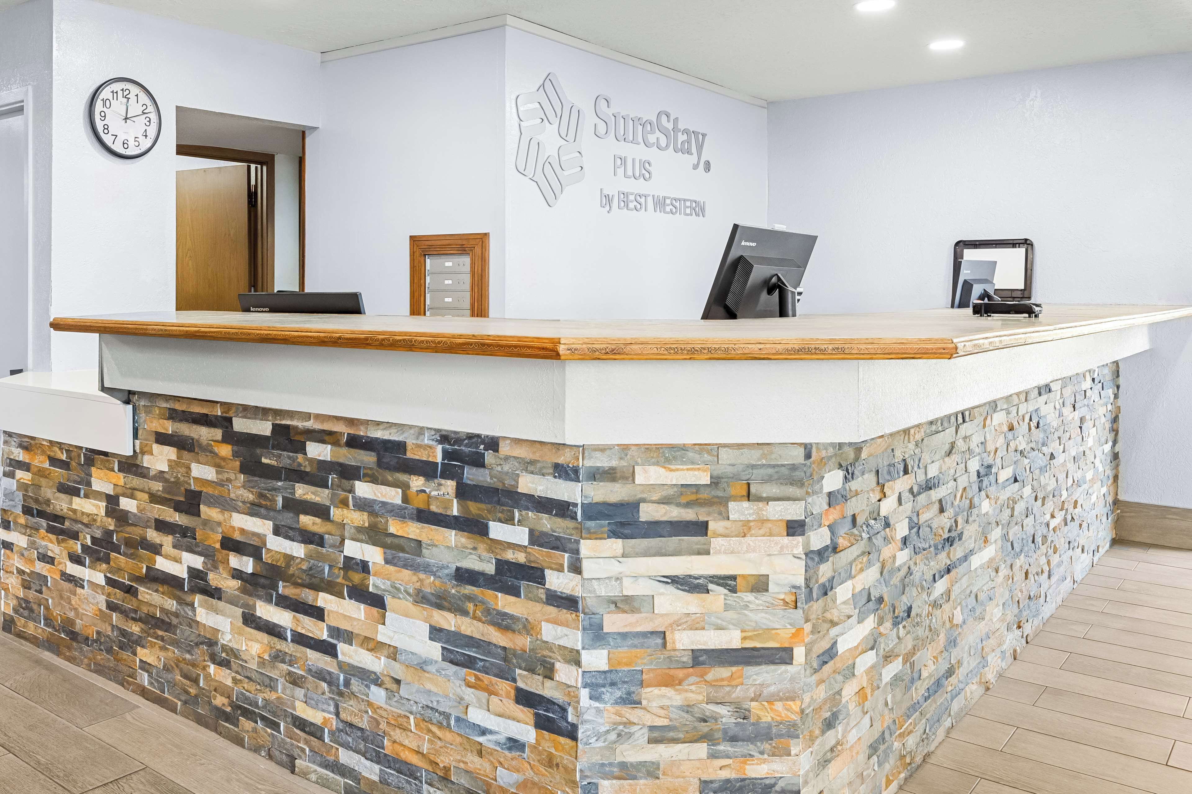 A reception area with a stone-patterned counter, a clock, and a sign that reads "SureStay Plus by Best Western."