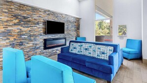 A modern living room with a stone wall, a flat-screen TV, a fireplace, and blue furniture.
