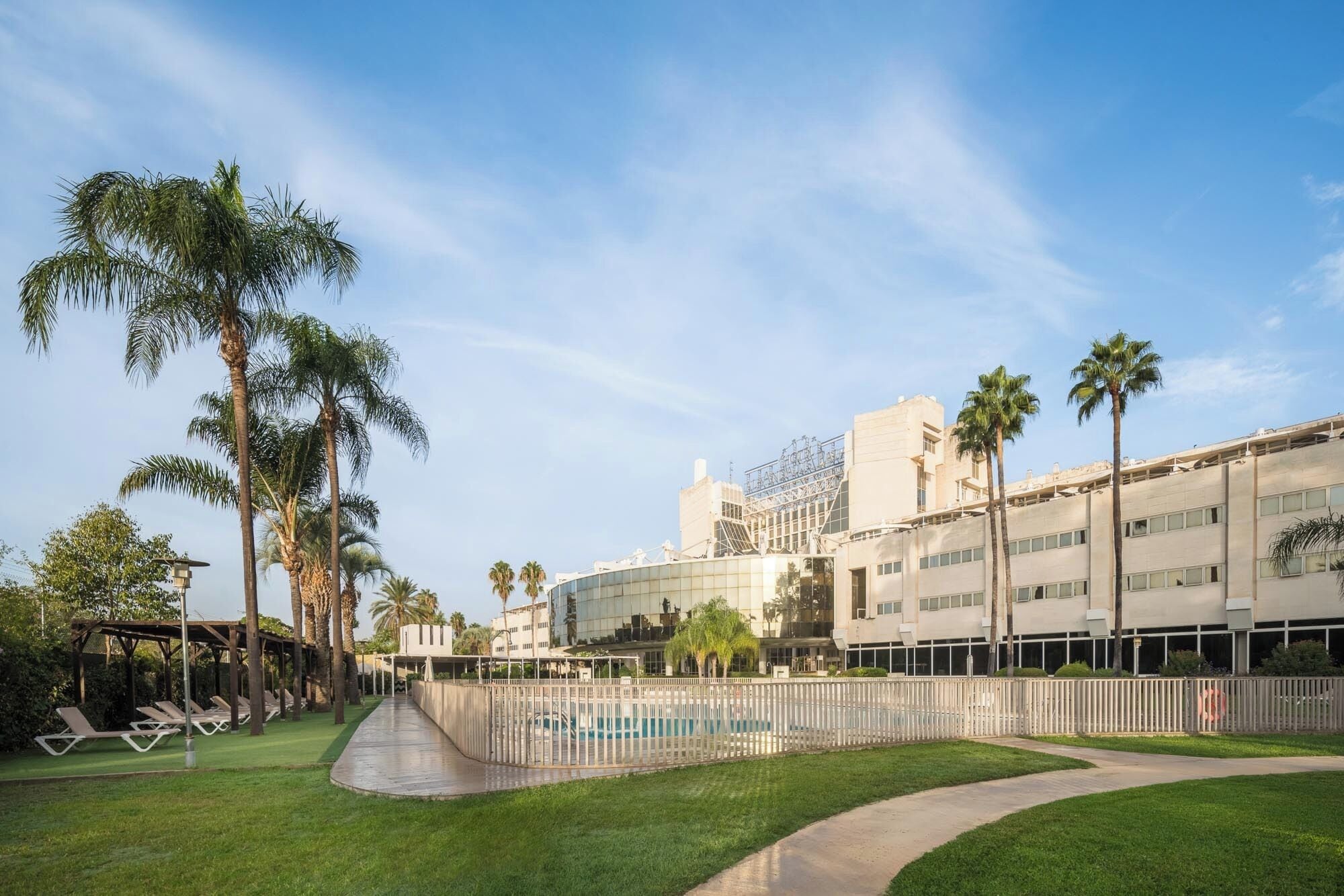 A hotel with a pool area, palm trees, and a modern building with a glass facade.