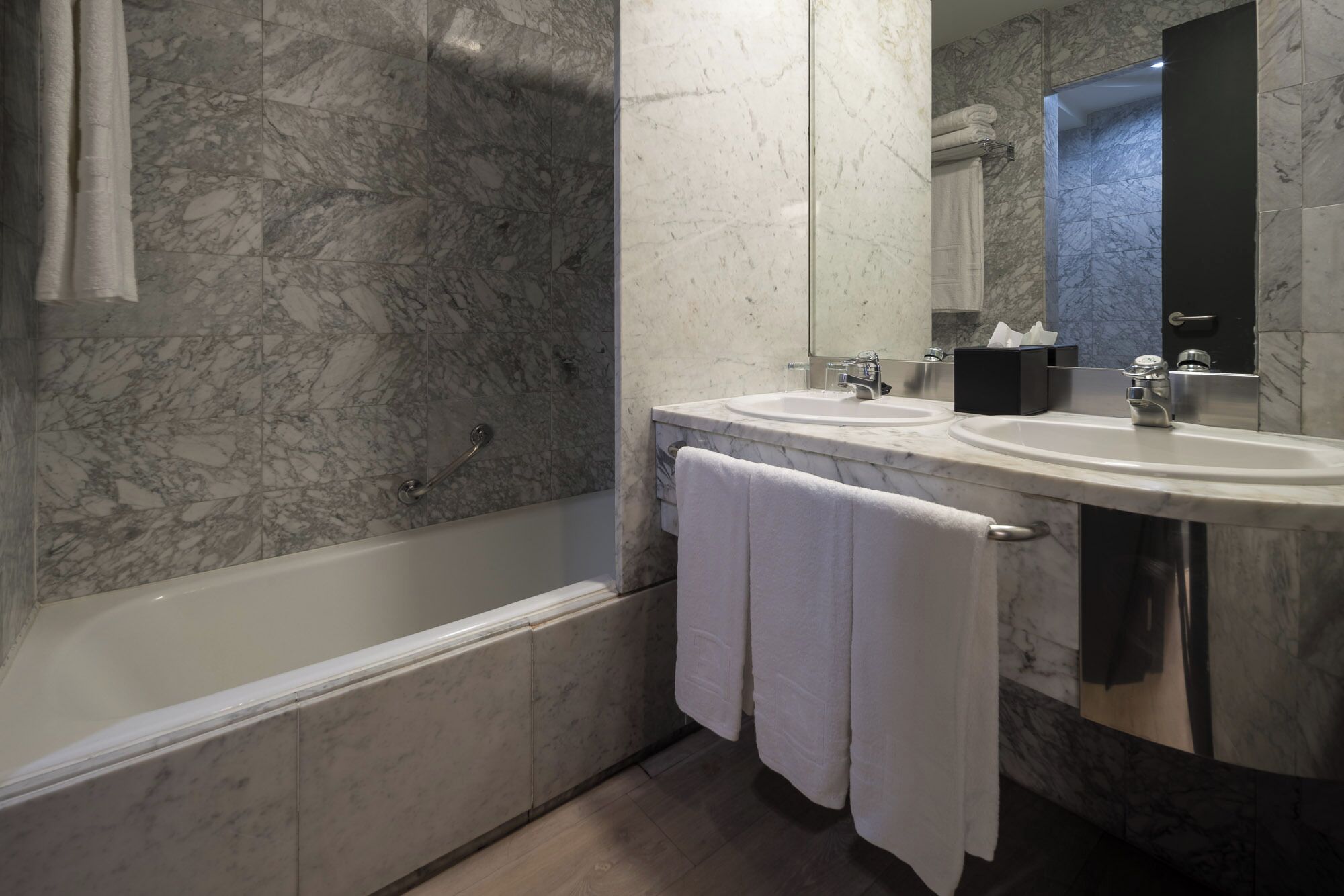 Un baño con bañera, dos lavamanos, un espejo y paredes de mármol.