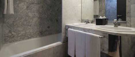 A bathroom with a bathtub, two sinks, a mirror, and marble walls.