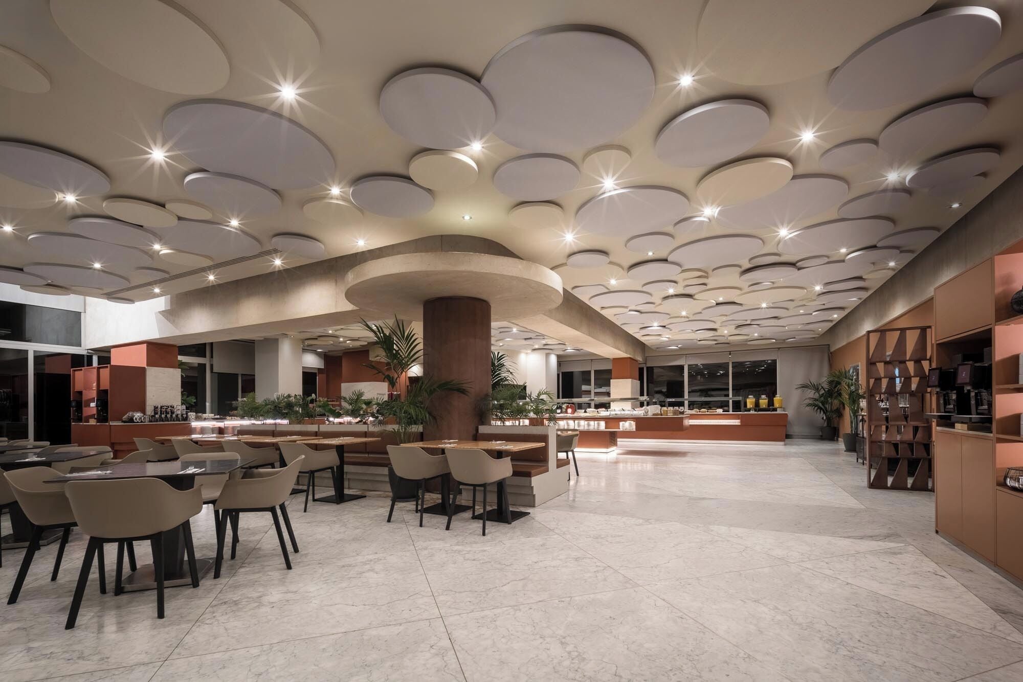 Un vestíbulo amplio con un diseño de techo moderno, una zona de estar central y una barra de café.