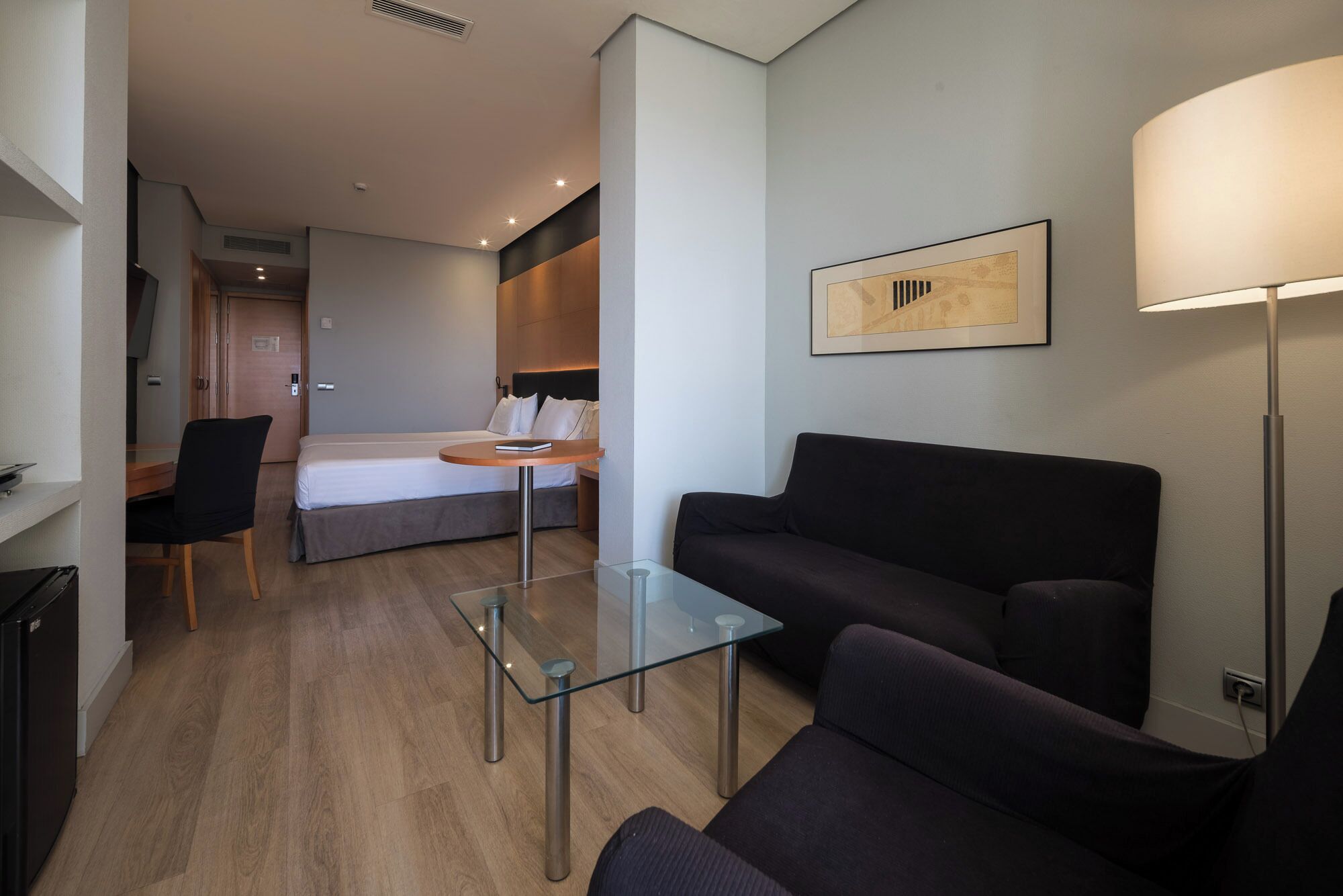 Une chambre d’hôtel moderne, équipée d’un lit, d’une table basse en verre, d’un canapé noir, d’un bureau et d’une lampe.