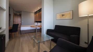Une chambre d’hôtel moderne, équipée d’un lit, d’une table basse en verre, d’un canapé noir, d’un bureau et d’une lampe.