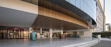 A modern hotel entrance with a curved facade, a spacious lobby, and a prominent staircase leading to the entrance.
