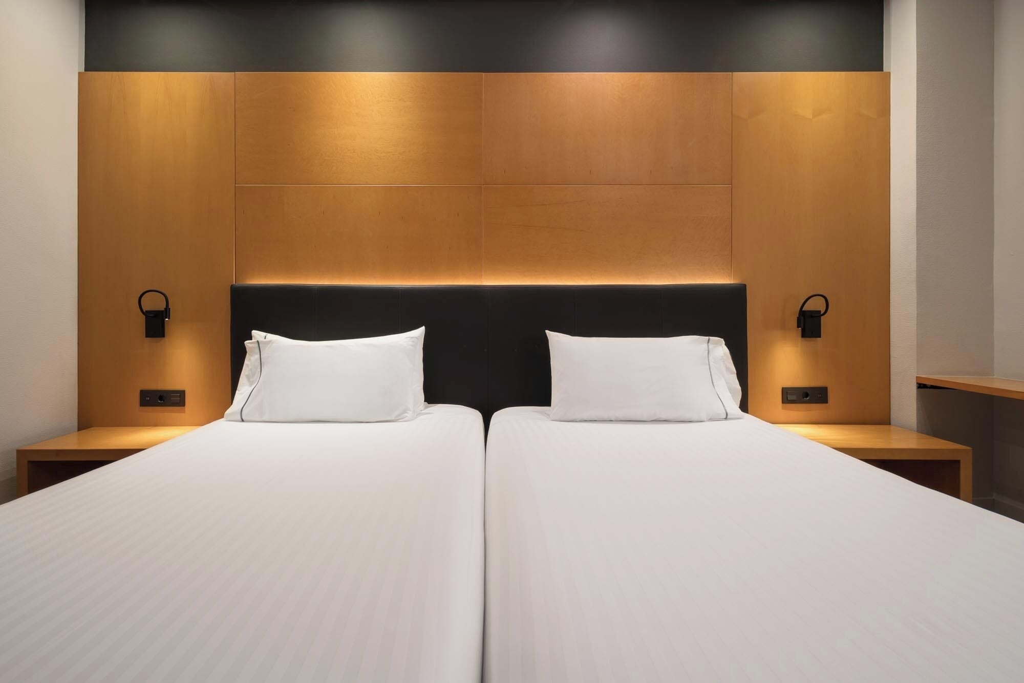 A double bed with a wooden headboard and two bedside tables, each with a wall-mounted lamp.
