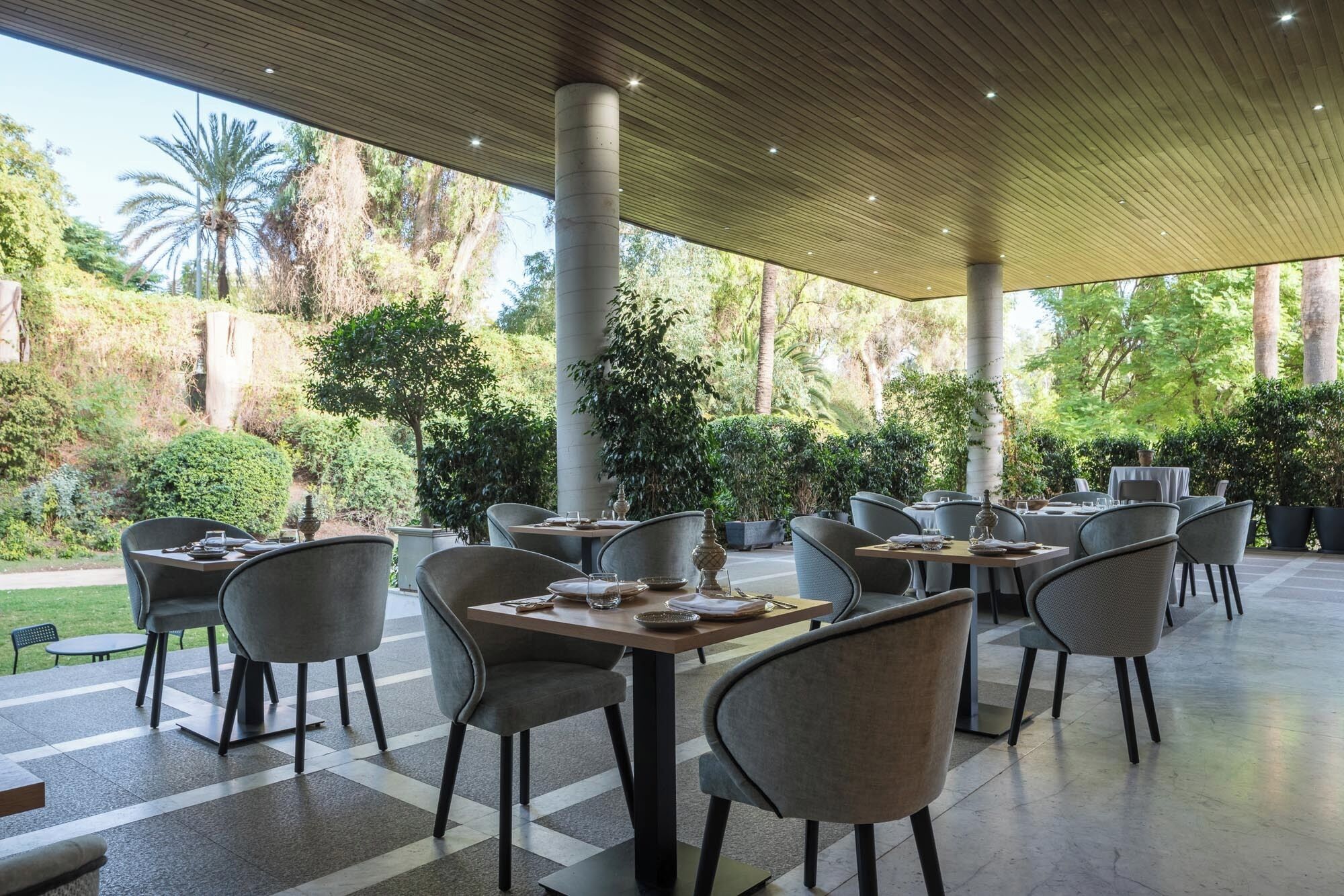An outdoor dining area with tables and chairs, surrounded by lush greenery and palm trees.