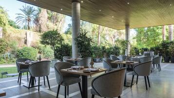 Un área de comedor al aire libre con mesas y sillas, rodeada de abundante vegetación y palmeras.
