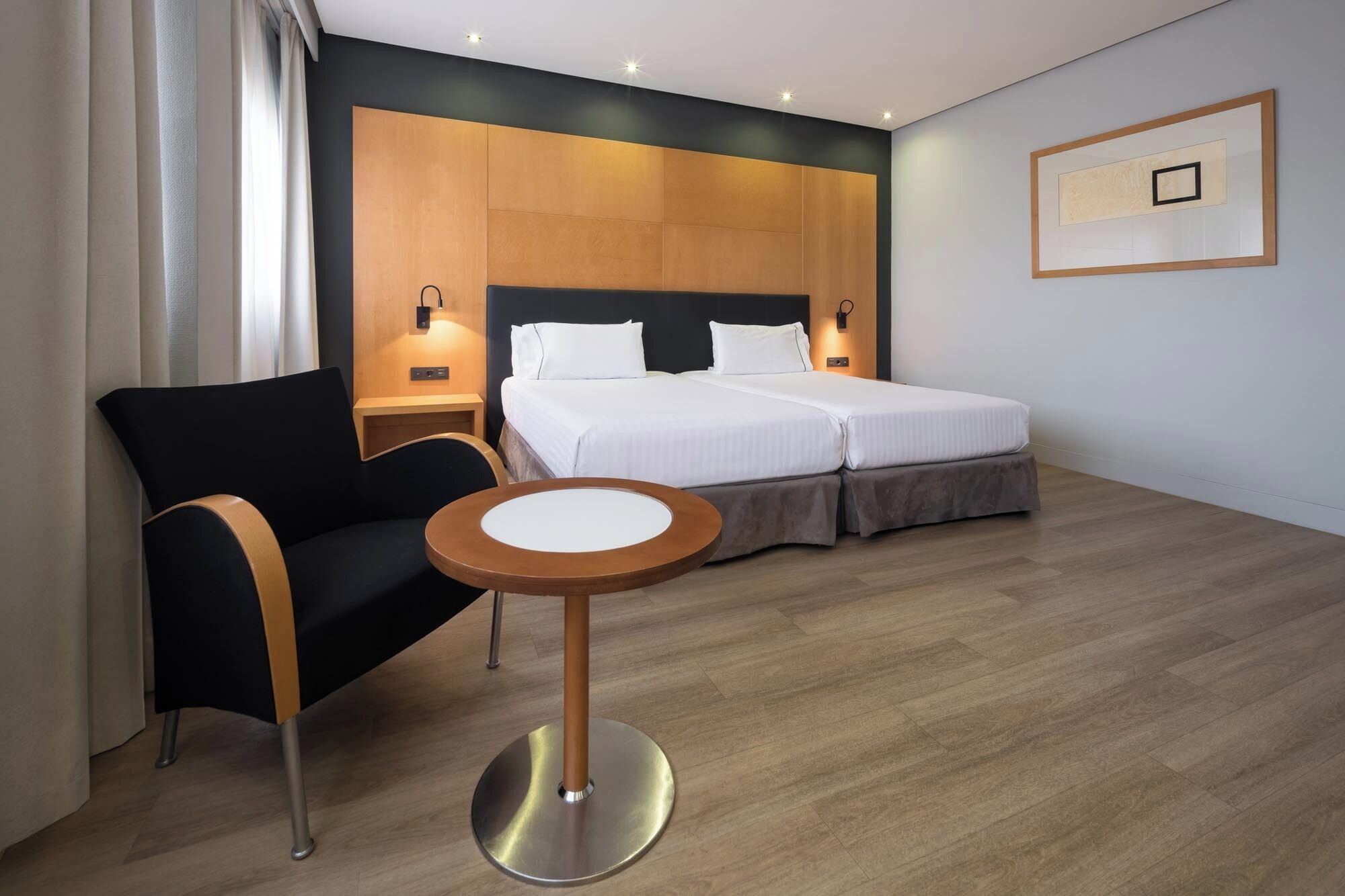 Une chambre d’hôtel avec un lit, une chaise, une petite table et un luminaire fixé au mur.