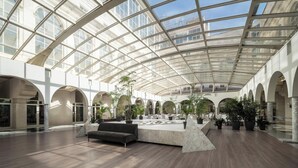 A spacious indoor area with a high ceiling and large windows, featuring a central seating area and multiple potted plants. - Eurostars Al-Ándalus Palace (Seville)