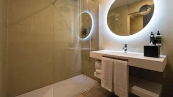 Un baño moderno con ducha envuelta en vidrio, un lavabo blanco y un espejo grande.