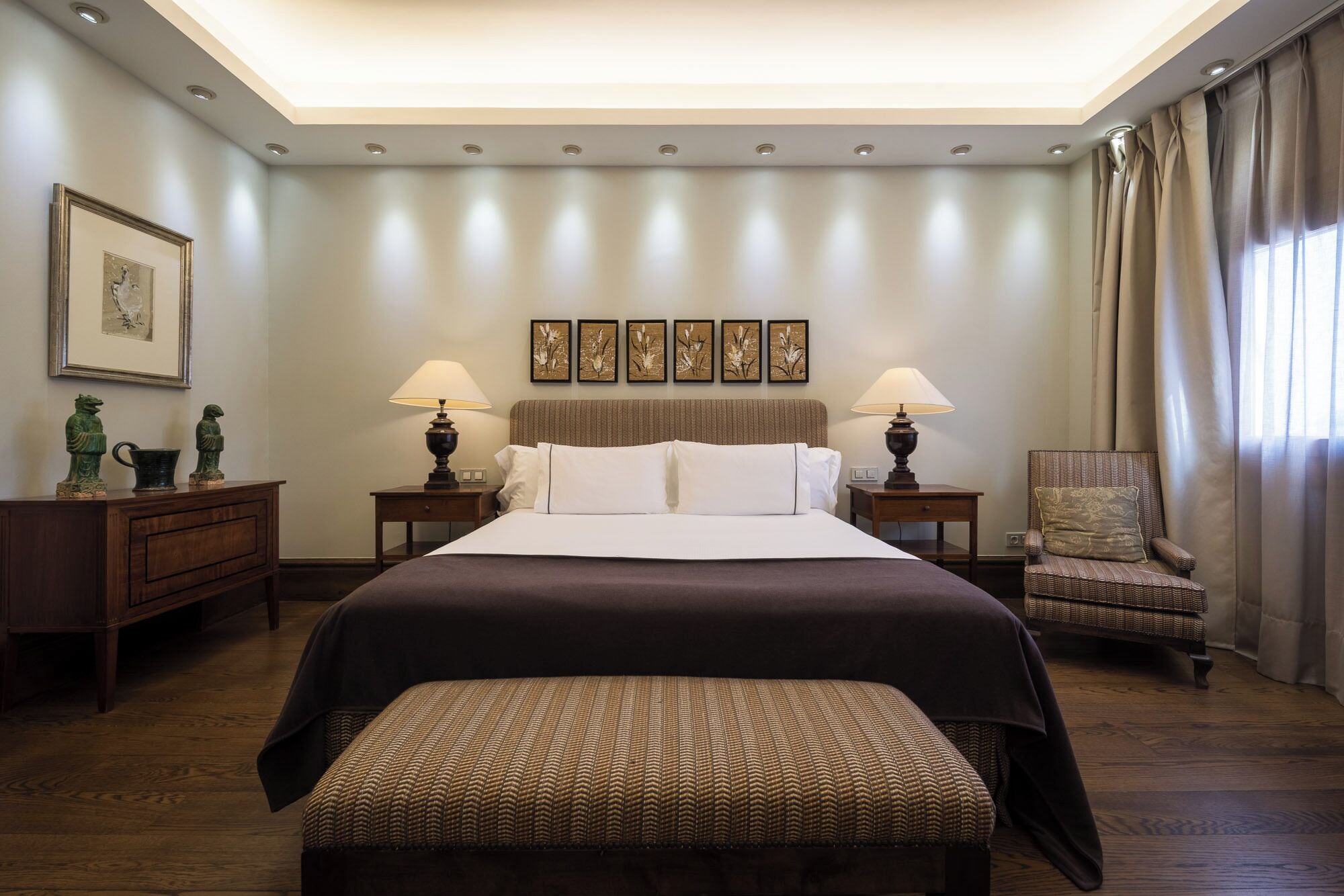 Una camera d'albergo luminosa con un letto grande, due comodini con lampade, una sedia e una panca.
