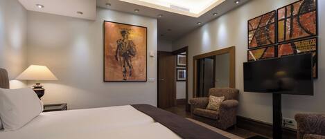 A hotel room with a large bed, two armchairs, a TV, and artwork on the walls.