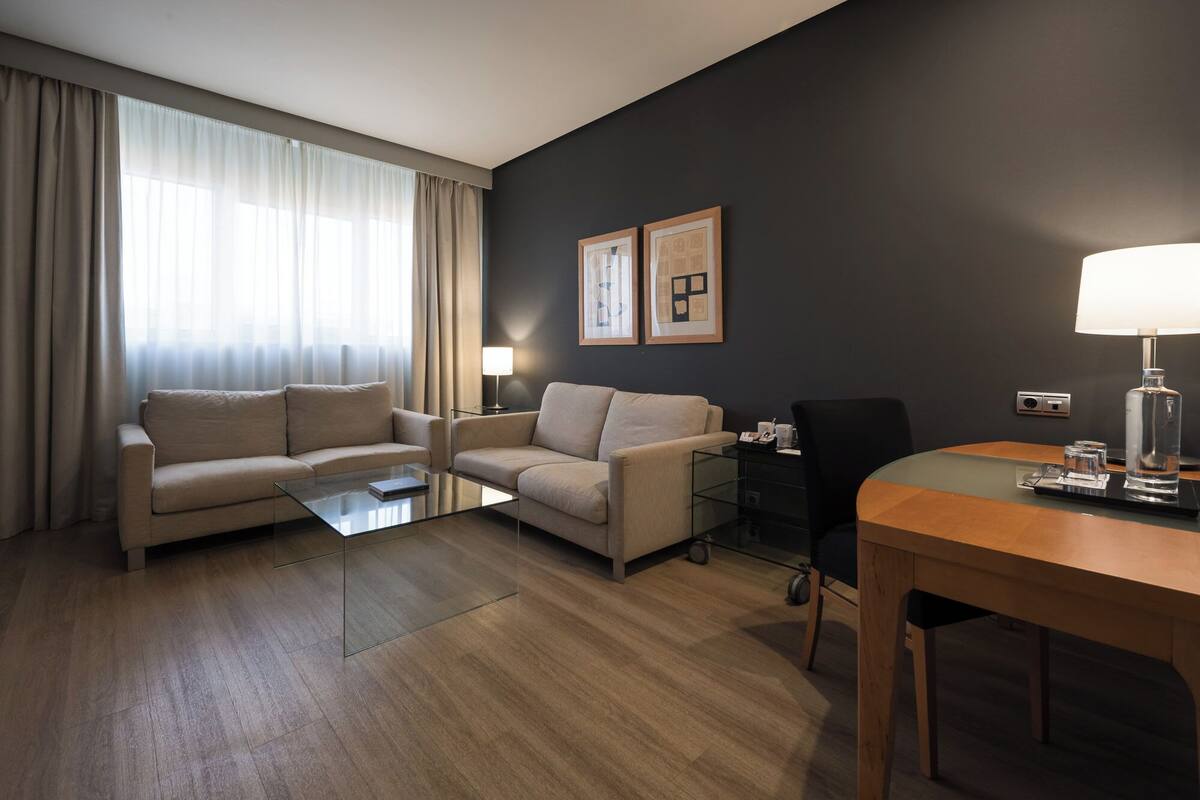 Una habitación de hotel con sofá, mesa de centro, mesa de comedor y lámpara.