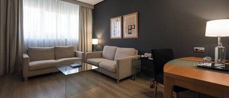 A hotel room with a sofa, a coffee table, a dining table, and a lamp.