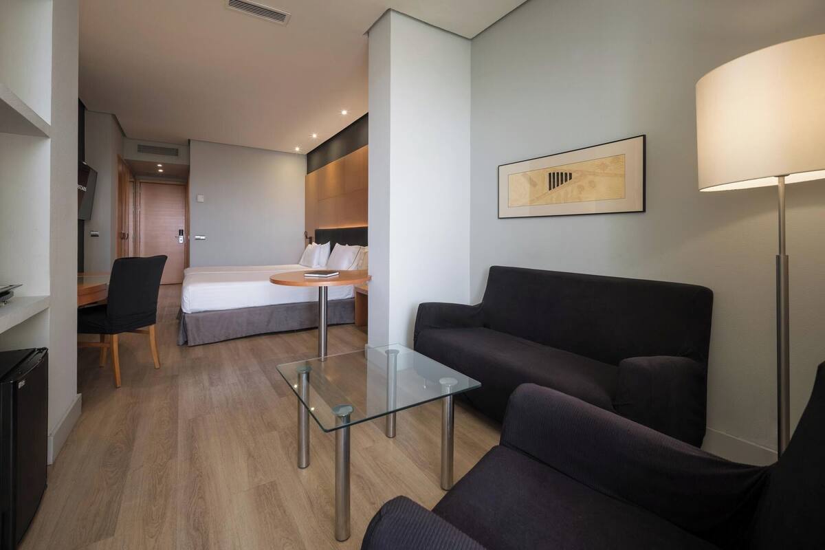 Una habitación de hotel moderna con una cama, una mesa de centro de cristal, un sofá, un escritorio y una lámpara.