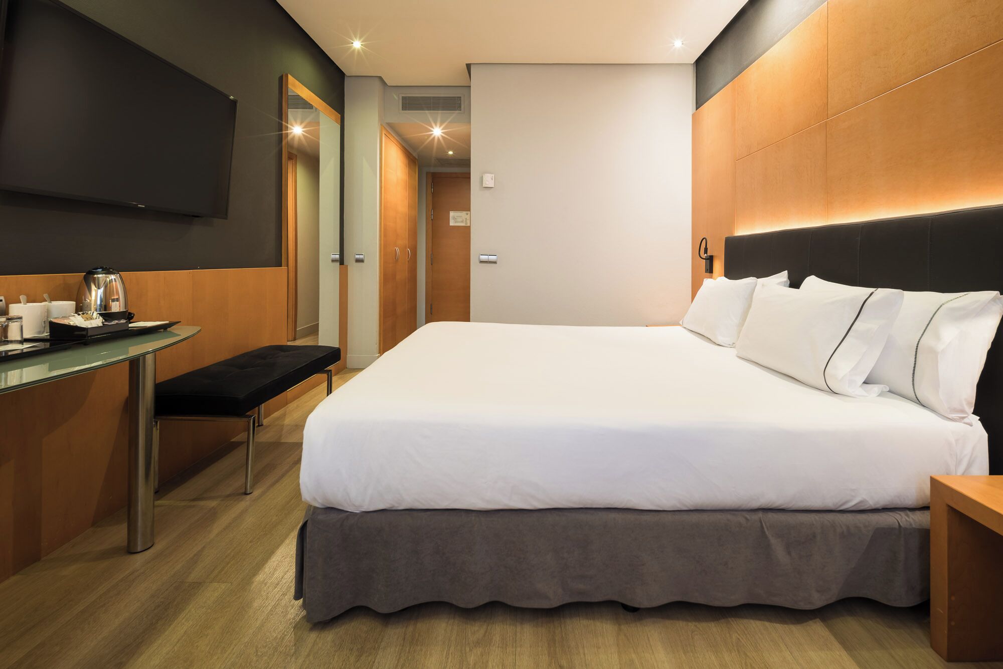 A hotel room with a bed, bedside table, and a desk with a coffee maker.