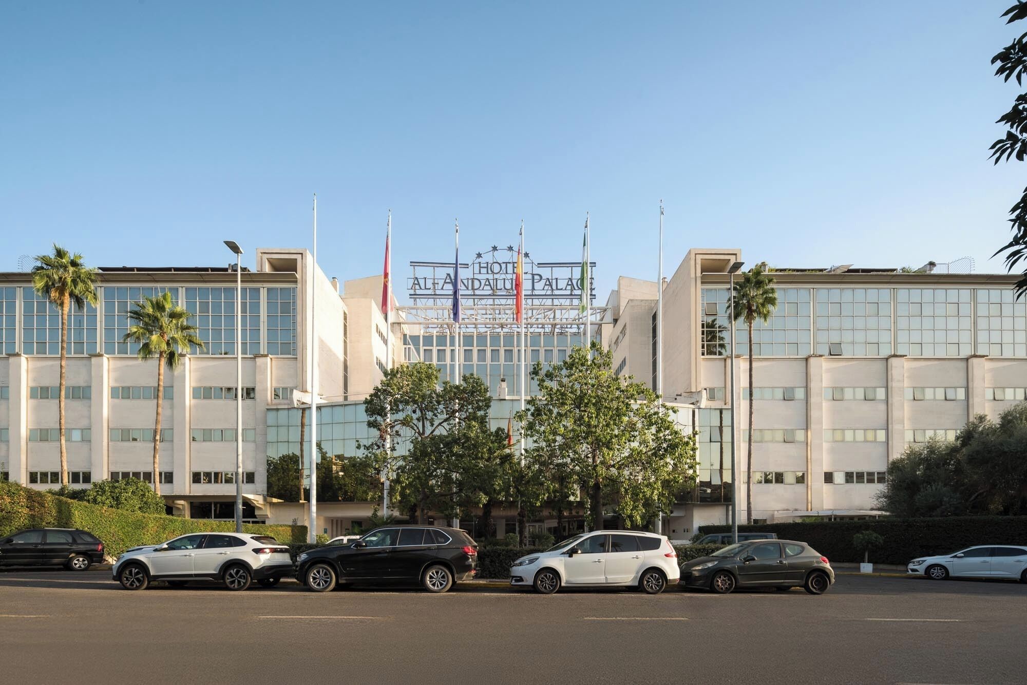 Un hôtel moderne, reconnaissable à son enseigne bien visible, à ses nombreux drapeaux et à son parking où sont stationnées plusieurs voitures.