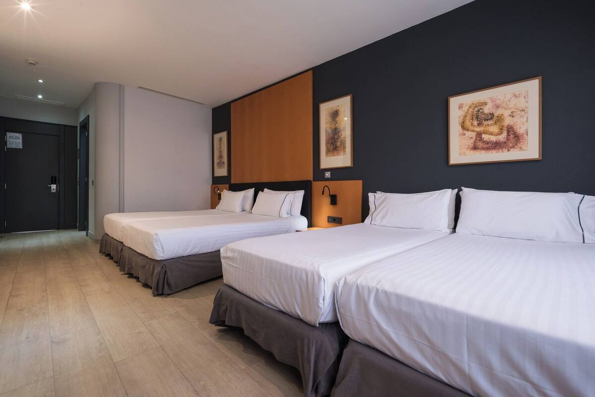 Una habitación de hotel con dos camas, piso de madera y obras de arte en las paredes.