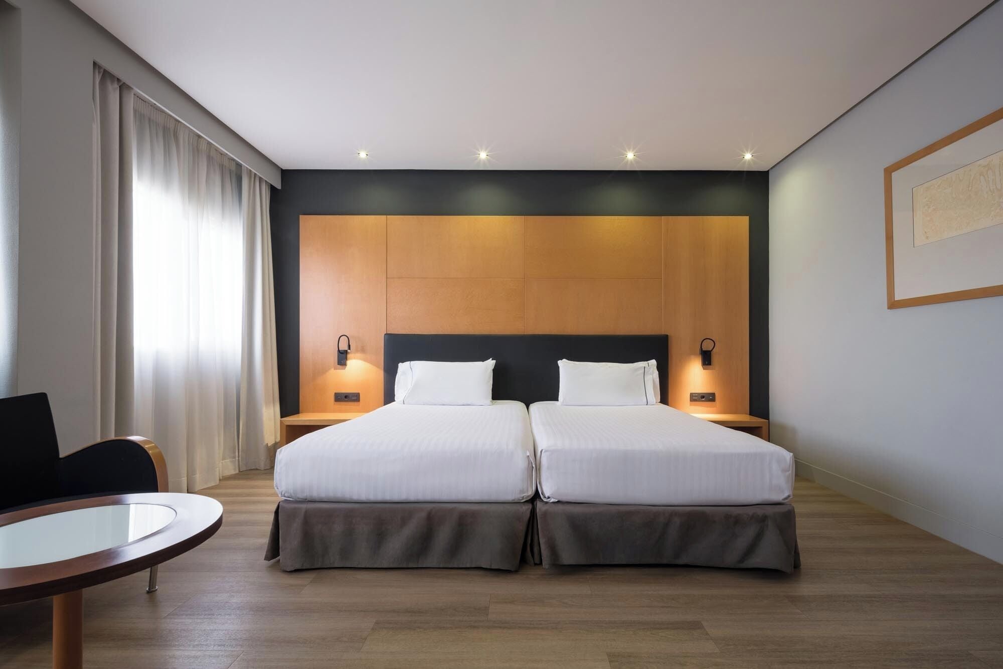 Habitación de hotel con dos camas, una mesita y una silla.