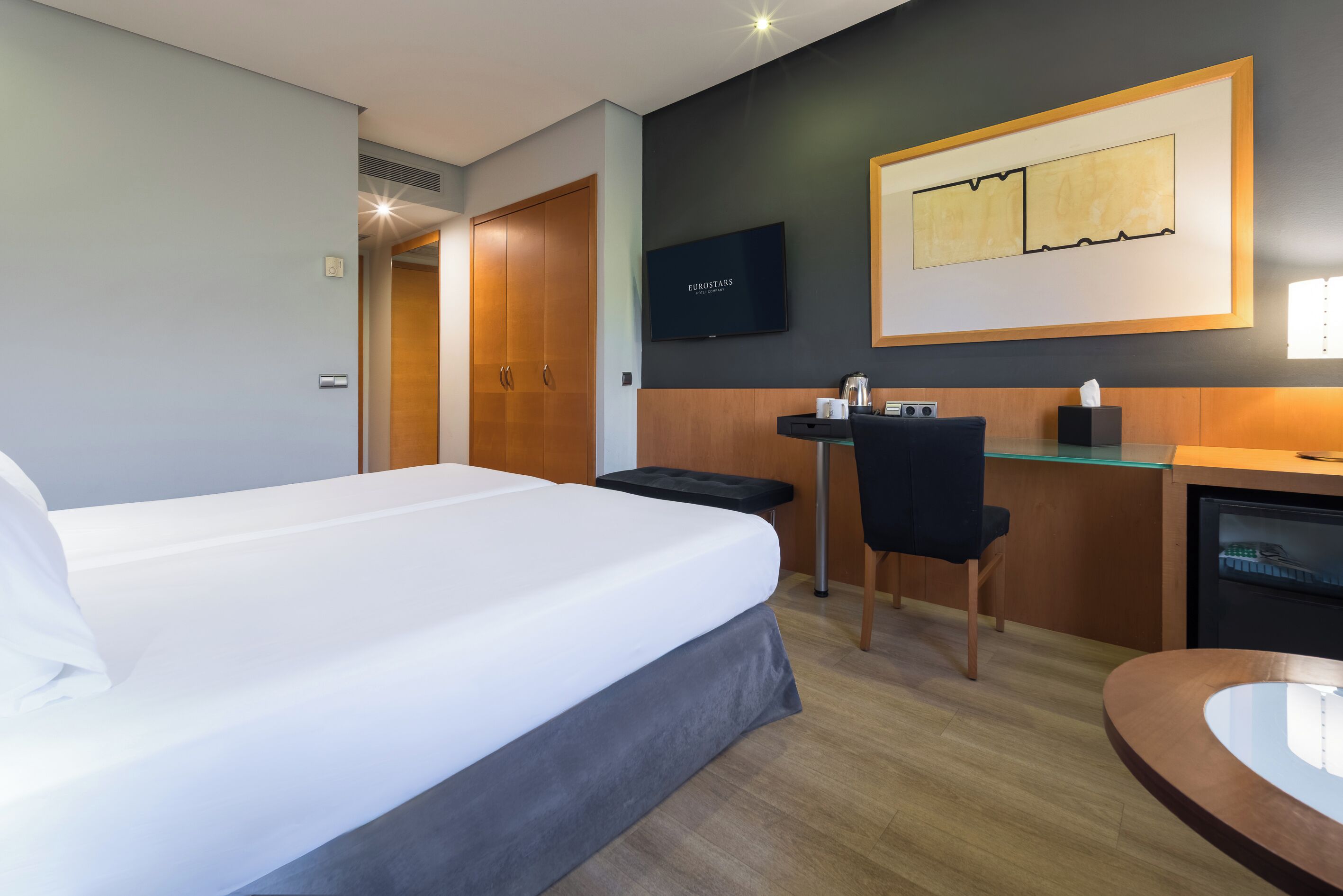 A hotel room with a bed, a desk, a chair, a television, and a small refrigerator.