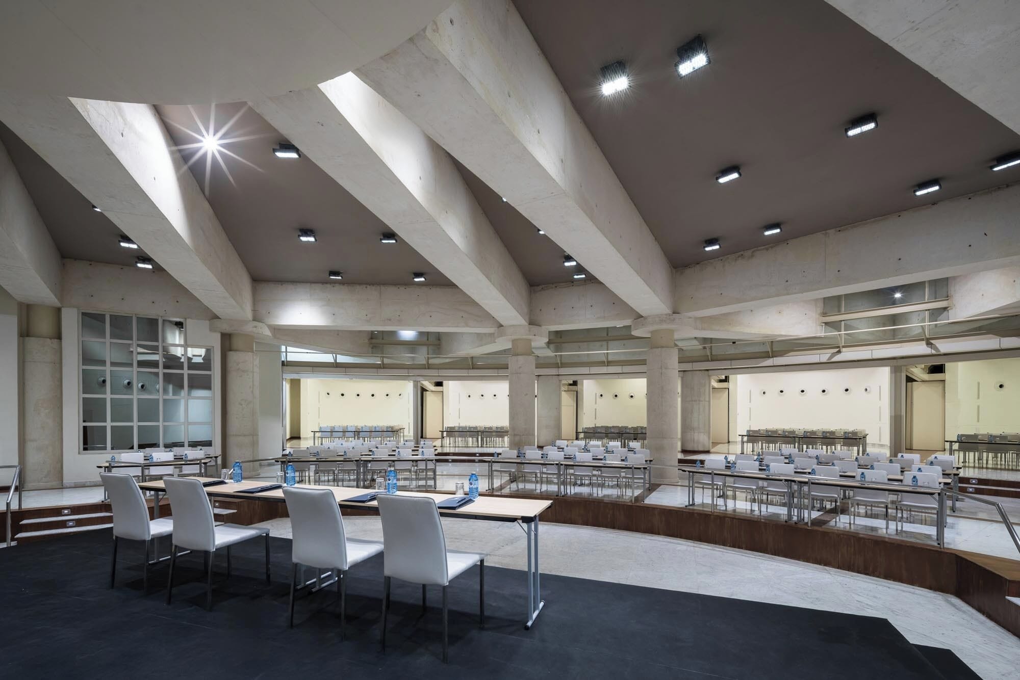 Un'ampia sala conferenze con soffitti alti, numerosi tavoli e sedie disposte per riunioni.