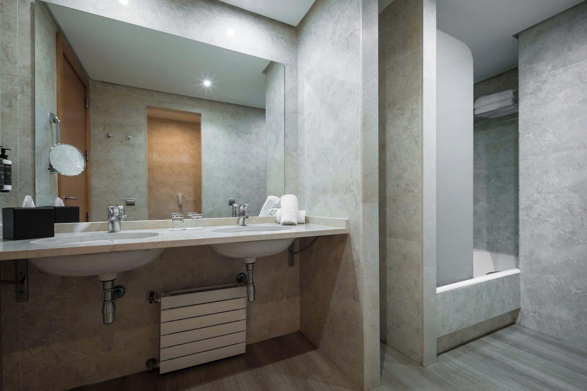 A modern bathroom with two sinks, a large mirror, and a walk-in shower.