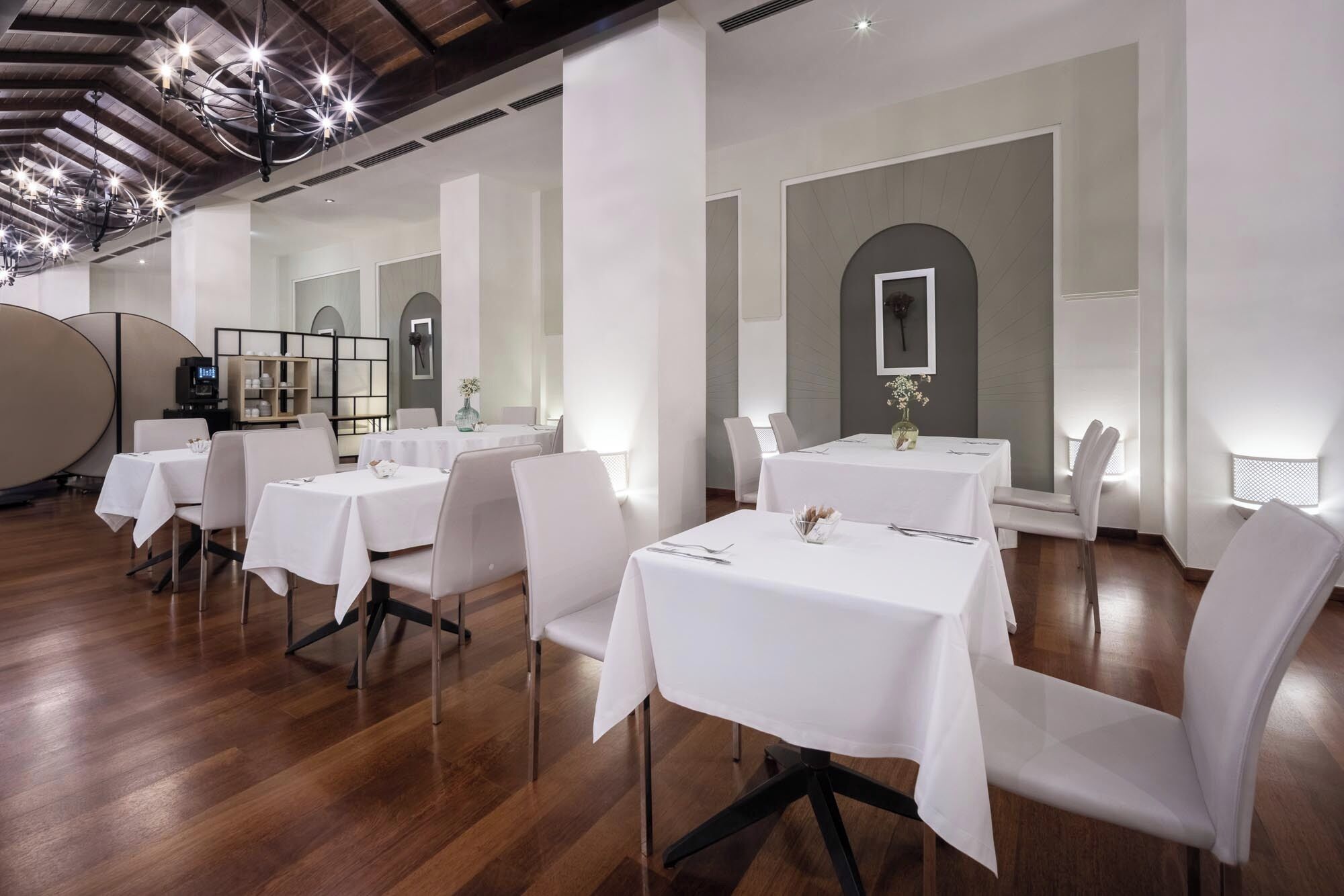 Un comedor con mesas redondas, sillas blancas y una lámpara moderna.