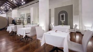 Un comedor con mesas redondas, sillas blancas y una lámpara moderna.