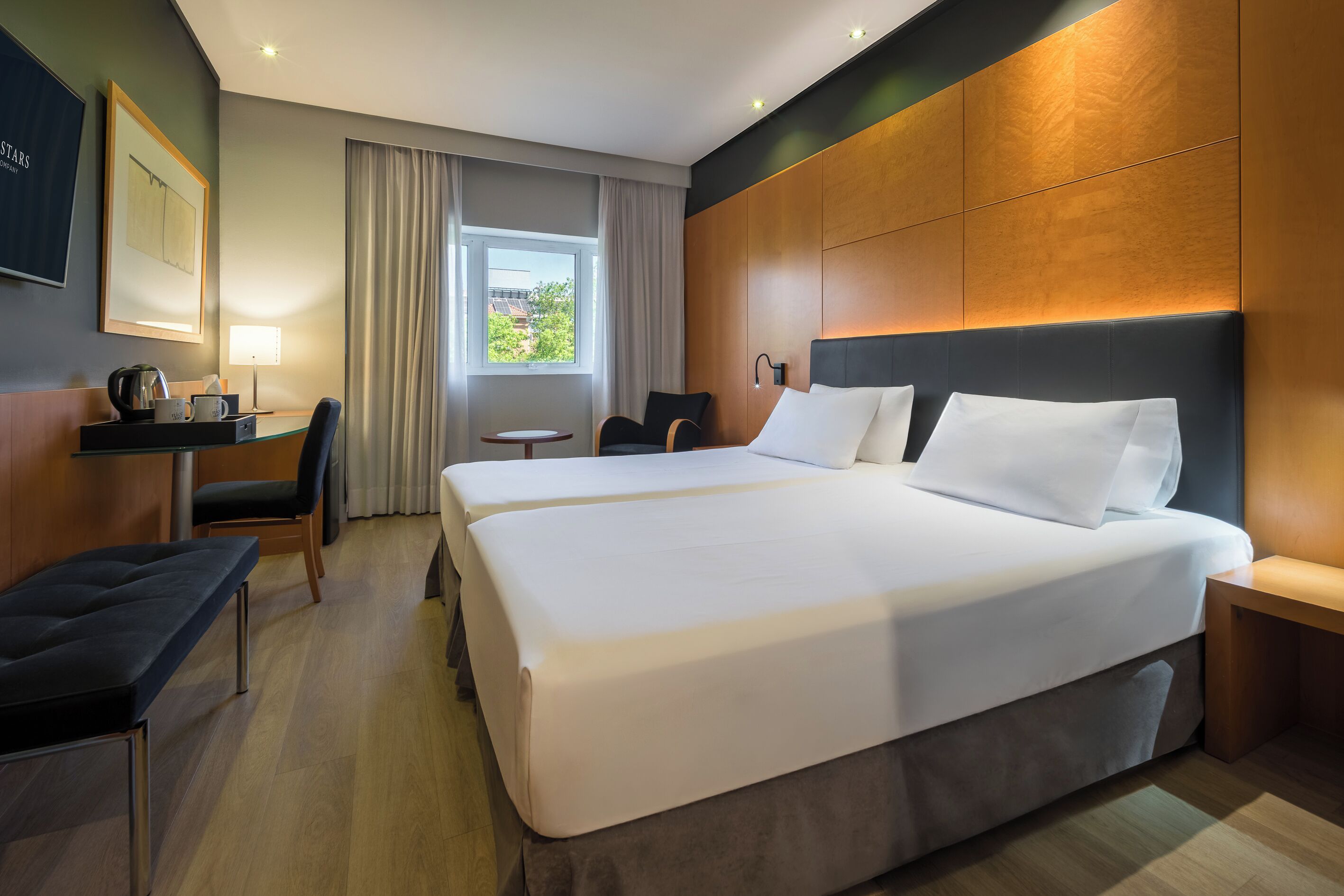 Habitación de hotel con una cama grande, un escritorio con lámpara, una silla y vistas al exterior.