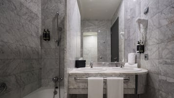 Uma casa de banho moderna com soalho de mármore, uma banheira, uma pia com bancada e um espelho.