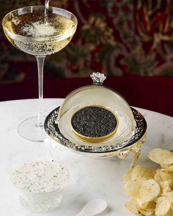 A martini glass with bubbles, a silver caviar dish, a small bowl of dip, and potato chips on a marble table.