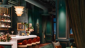 A bar area with a green sofa, red chairs, and a bar counter with bottles. - Beacon Grand, A Union Square Hotel  (San Francisco)