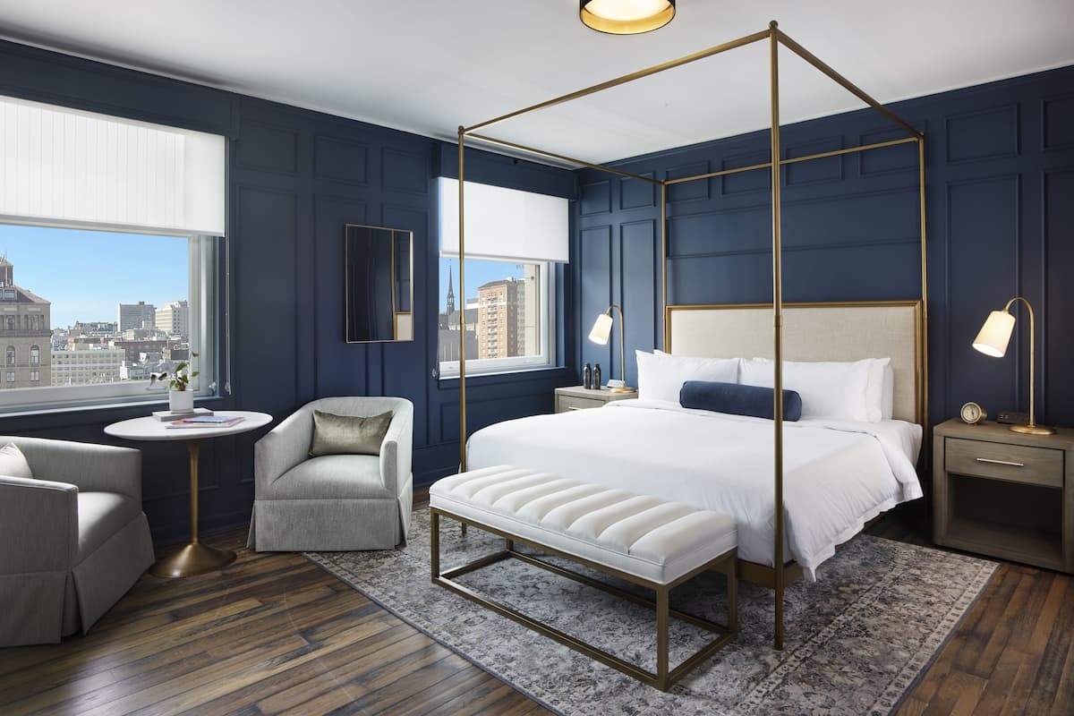 A modern bedroom with a four-poster bed, a city view, a round table, and a chair.
