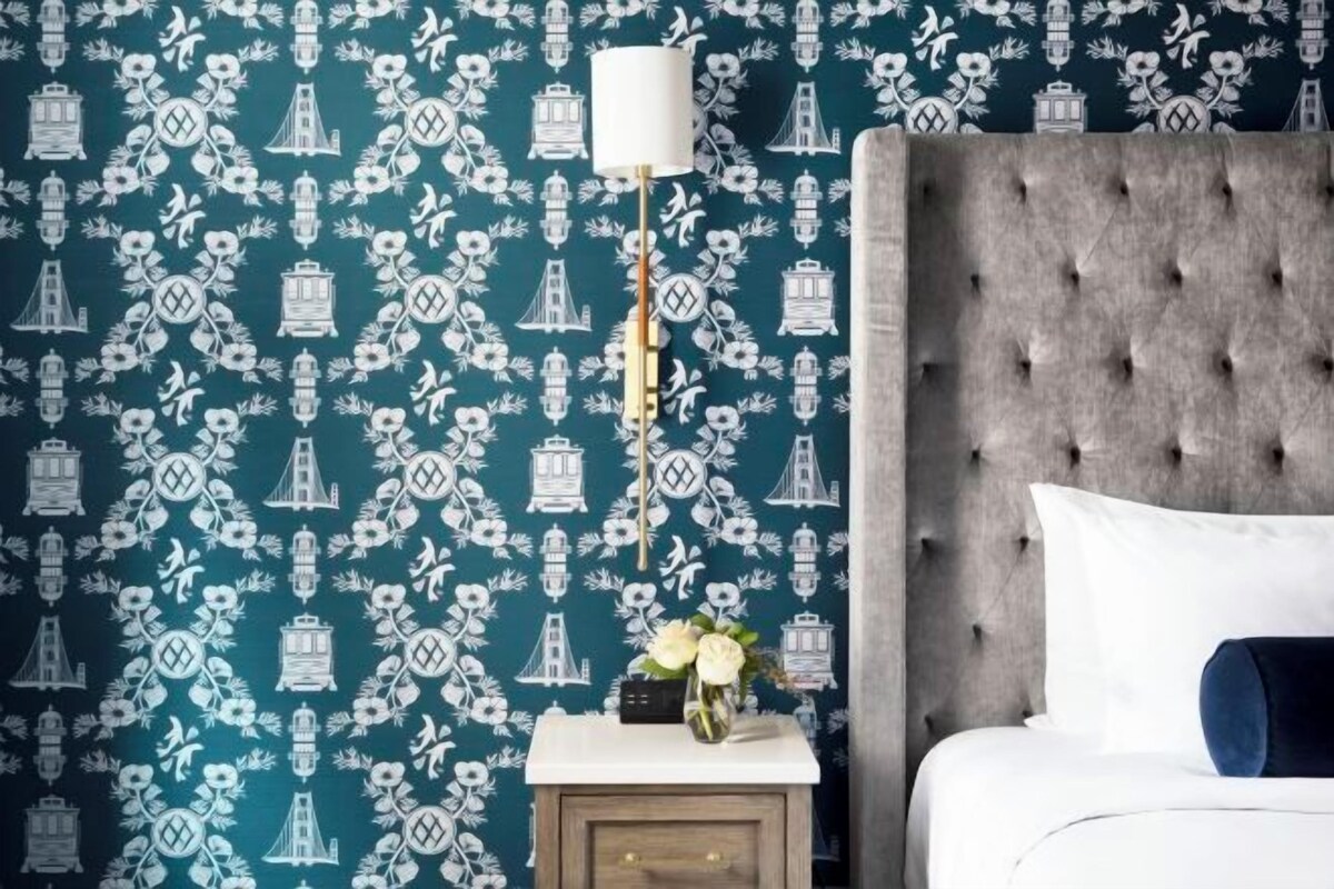 A bedroom with a tufted headboard, a bedside table with a lamp, and a floral wallpaper pattern.
