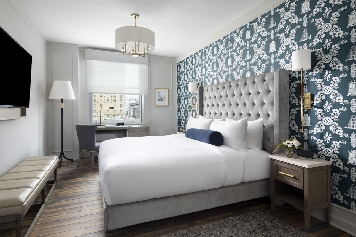 A modern hotel room with a large bed, a desk, and a view of the city through the window.