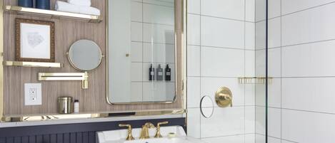 A bathroom with a white toilet, a sink with gold fixtures, a mirror, and a shower area.