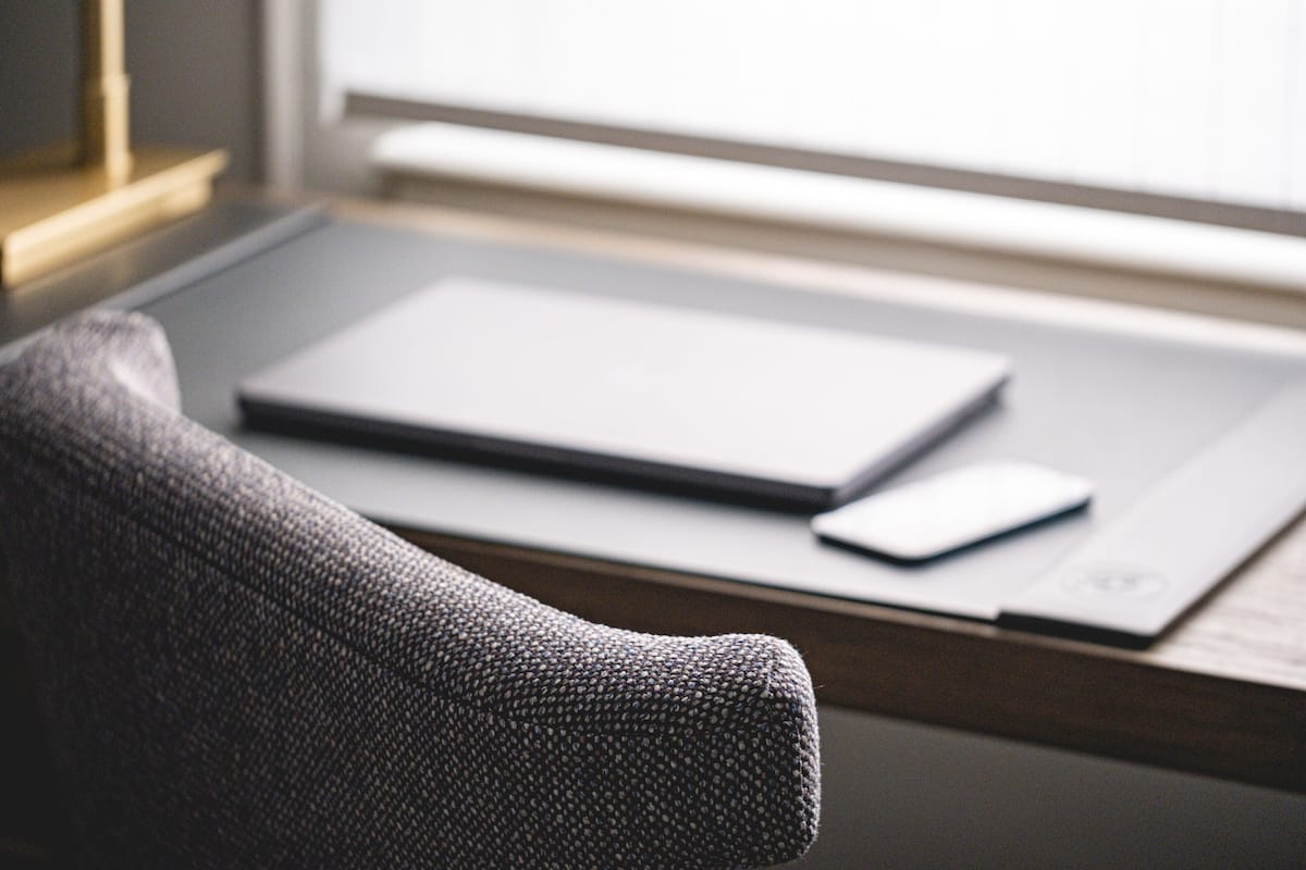 A laptop on a desk near a window, with a chair partially visible.