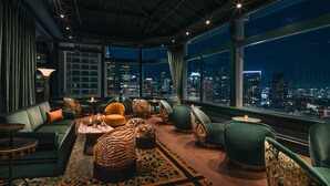 A high-rise hotel room with a city view, leather sofas, patterned ottomans, and a leopard print rug. - Beacon Grand, A Union Square Hotel  (San Francisco)