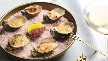 A plate of oysters on the half shell with a pink salt bed, a lemon half, and a red pepper flake.