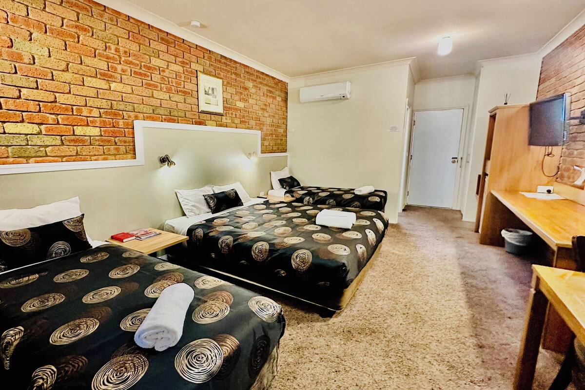 A hotel room with two beds, a brick wall, a television, and a desk.