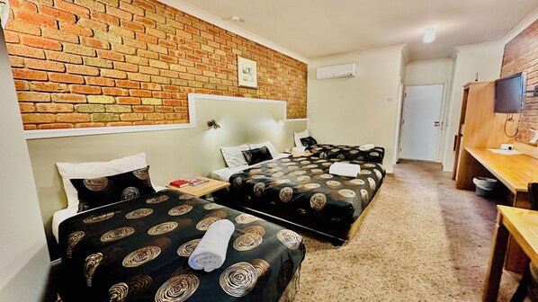 Une chambre d’hôtel avec deux lits, un mur en briques, une télévision et un bureau.